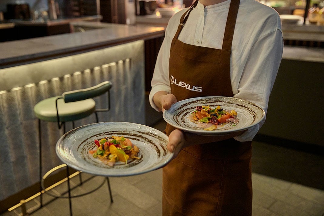 Wait staff wearing 'Lexus' apron serving two plates of fine dining food as part of Lexus Encore Fine Dining.